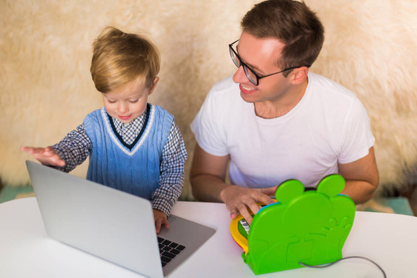 Le jeune père heureux avec son petit fils mignon en utilisant des ordinateurs portables à l'intérieur
 - Photo, image