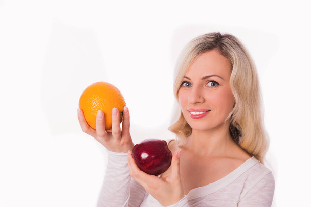 Portrait of young divine blonde woman who keeping orange and apple in hands against the white background - Foto, immagini