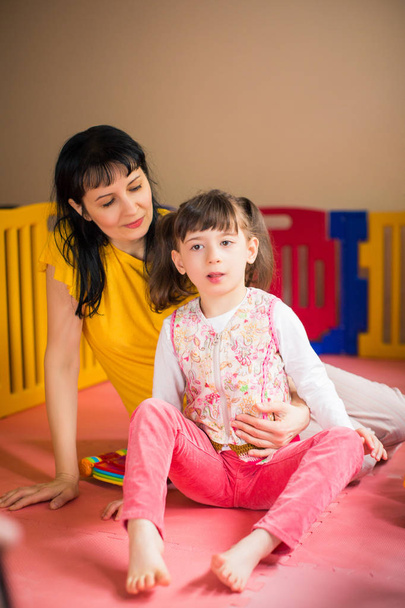 The little beautiful disabled girl sitting near young happy mother in the room - 写真・画像