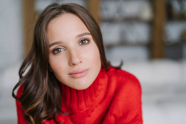 Headshot of attractive healthy European woman with dark hair and soft skin, looks directly at camera, wears warm red sweater, models indoor. People and lifestyle concept. Domestic atmosphere - Photo, Image