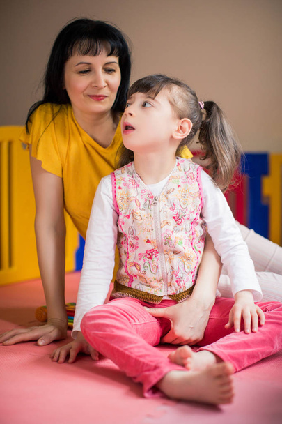 The little beautiful disabled girl sitting near young smiling mother in the room - Foto, afbeelding