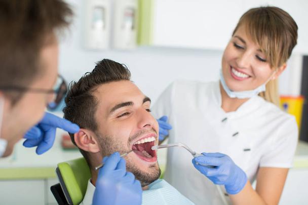 Dentist and nurse making professional teeth cleaning to male young patient at the dental office. - 写真・画像