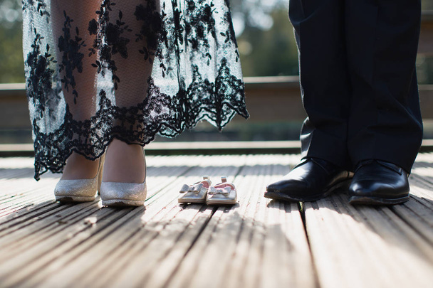 Detailní záběr nohou ženy v botách, nohy člověka v botách a malá obuv mezi nimi - Fotografie, Obrázek