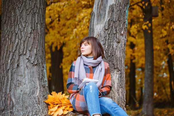 University Park, study concept. Portrait of young woman in fall forest . Writes in a notebook. Brunette woman in autumn park with fashionable plaid coat and scarf. - Photo, Image