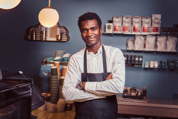 Portrait of a handsome African barista standing with crossed arms at counter of a trendy coffee shop. - Photo, Image