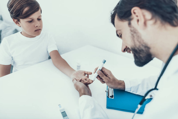Doctor Taking Blood Sample from Boy's Finger. Diabetes Concept. Sugar in Blood. Healthcare Concept. Young Man in Uniform. White Coat. Medical Equipment. Boy in Clinic. Glucometer in Hand. - Foto, Imagem
