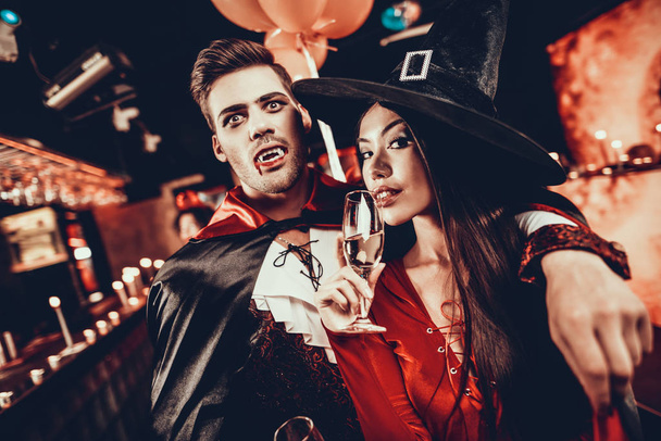 Young Happy Couple in Costumes at Halloween Party. Handsome Man and Beautiful Woman Drinking Champagne at Halloween Party in Nightclub. Friends having Fun. Celebration of Halloween - Foto, Imagem