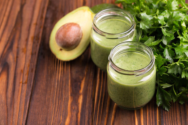 Fresh spinach and avocado smoothie in glass jars with parsley on rustic wooden background. Horizontal view. Copy space - Photo, Image