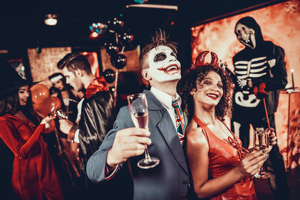 Young Smiling Couple in Halloween Costumes Dancing. Handsome Man and Beautiful Woman Drinking Champagne and Dancing at Halloween Party in Nightclub. Friends having Fun. Celebration of Halloween - Photo, Image