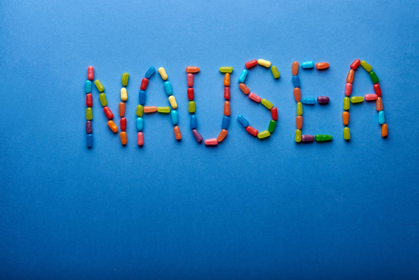 La parola "nausea" è messa fuori da targhe multicolori, vitamine, caramelle di gelatina. Annunciatore di vomito. Il problema con il corpo dopo il cibo, intossicazione chimica
. - Foto, immagini