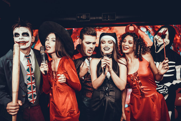 Young People in Halloween Costumes Singing Karaoke. Happy Smiling Friends Wearing Costumes having Fun by Singing with Microphone at Halloween Party in Nightclub. Celebration of Halloween - Foto, Bild