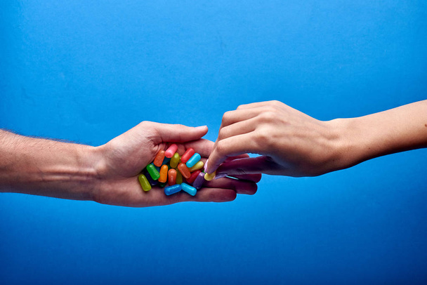 La mano di una donna prende una piccola caramella gelatina da un uomo. Molti farmaci multicolori per la terapia terapeutica contro le malattie in un paziente malato. Pillole gialle, viola, arancioni, rosse, blu, verdi, rosa
. - Foto, immagini