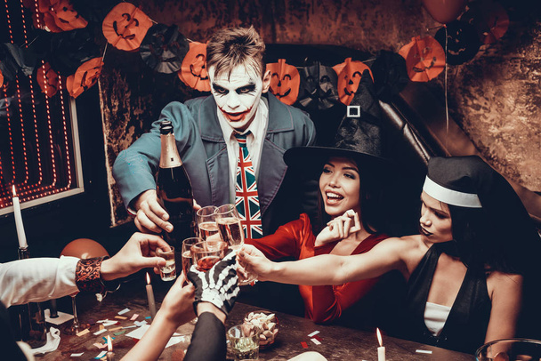 Young Smiling People in Costumes Clinking Glasses. Group of Young Happy People Wearing Costumes at Halloween Party Sitting at Table and Drinking Champagne. Celebration of Halloween - Foto, Imagen