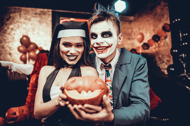Portrait of Young Couple in Halloween Costumes. Beautiful Woman and Handsome Young Man Wearing Costumes holding Pumpkin at Halloween Party in Nightclub. Happy Friends having Fun Celebrating Halloween - Φωτογραφία, εικόνα