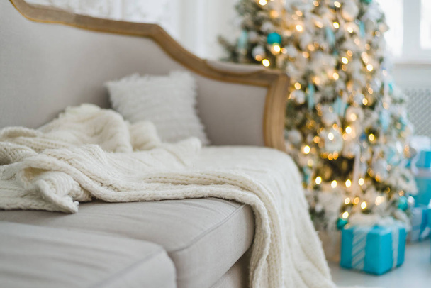 Kerst of nieuwjaar decoratie bij Woonkamer interieur en vakantiehuis decor concept. Rustig beeld van deken op een vintage bank met boom, liften, geschenken. Selectieve focus - Foto, afbeelding