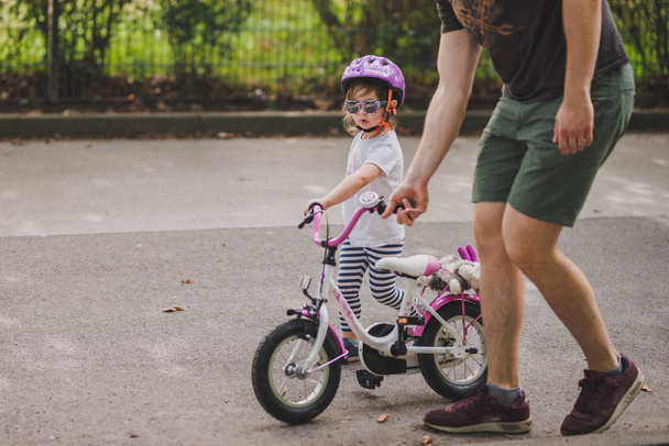 toddler girl with her father walk down the street and roll a bike - Fotoğraf, Görsel