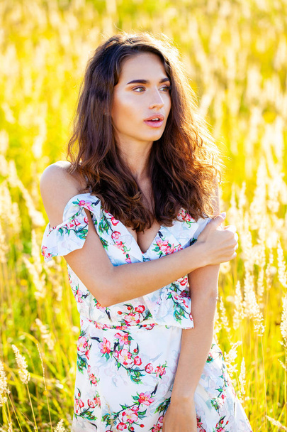 Portrait close up of young beautiful brunette woman in white dress, posing at sunset in the field - Φωτογραφία, εικόνα