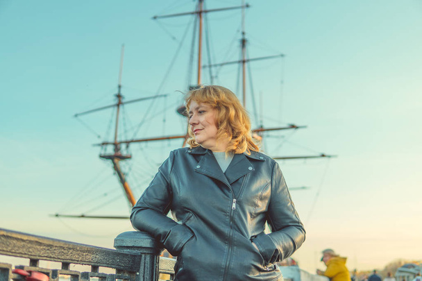 Adult woman posing on the waterfront, on the background of water and historical ship. - Foto, afbeelding