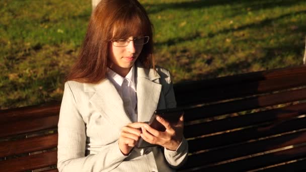 hermosa mujer de negocios con gafas comprueba el correo electrónico en la tableta en el parque en un banco
 - Imágenes, Vídeo