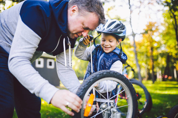 Día del Padre Papá caucásico e hijo de 5 años en el patio trasero cerca de la casa en la hierba verde en el césped reparando una bicicleta, bombeando una rueda de bicicleta. Papá enseña a reparar la bicicleta de un niño
. - Foto, Imagen