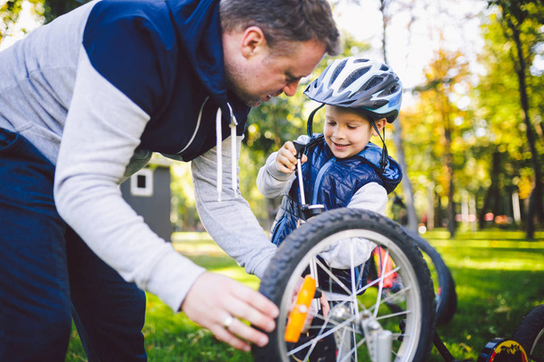 Babalar günü beyaz baba ve arka bahçesinde 5 yaşındaki oğlu bir bisiklet tamir çim yeşil çimlere şirketten bir bisiklet tekerleği pompalama yakın. Baba Çocuk Bisiklet tamir öğretir. - Fotoğraf, Görsel