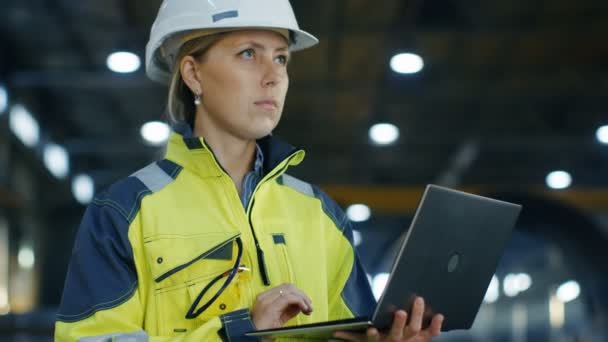 Portrét ženy inženýr v Hard Hat používá přenosný počítač stoje v továrně vyrábějící těžkého průmyslu. V pozadí projektu různé zámečnické díly ležící - Záběry, video