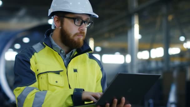 Industrial Engineer in Hard Hat Wearing Safety Jacket Uses Laptop. He Works in the Heavy Industry Manufacturing Factory with Various Metalworking Processes are in Progress. - Footage, Video