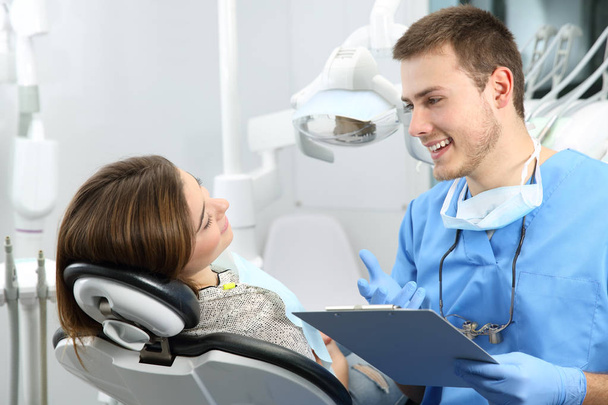 Young dentist explaining dental treatment procedure to a patient in a consultation - Foto, Bild