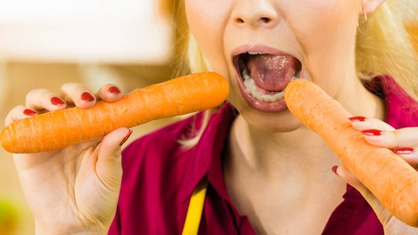 Vegetable having good impact on teeth. Young woman eating biting orange delicious carrot. - Foto, afbeelding