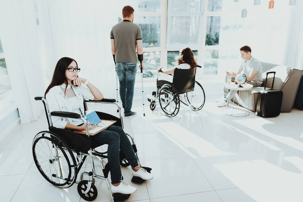 People in Wheelchair. Disabled in Hall. Woman in Wheelchair. Man on Crutches. Room with Panoramic View. Gray Sofa. White Interior. Airport Lounge. Limited Opportunities. Disabled in Airport Lounge. - Foto, Imagem