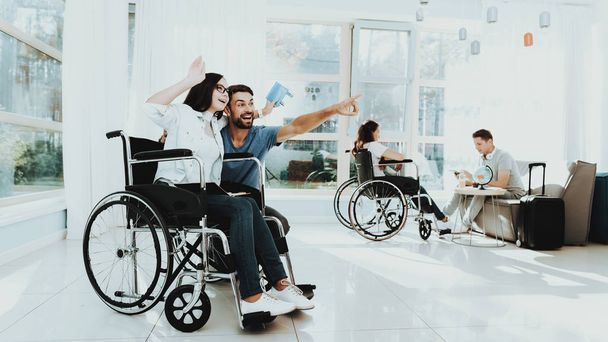 People in Wheelchair. Disabled in Hall. Woman in Wheelchair. Man on Crutches. Room with Panoramic View. Gray Sofa. White Interior. Smiling Man and Woman Disabled. Limited Opportunities. Airport Hall. - Fotoğraf, Görsel