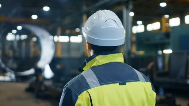 Industrieel ingenieur in Hard Hat en veiligheidsvest kijkt rond in grote zware industrie Manufacturing fabriek. Arc View beeldmateriaal. - Video
