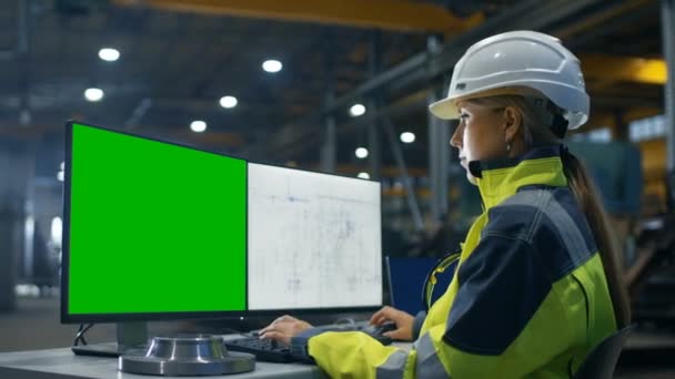 Uvnitř těžkého průmyslu výroby ženské inženýr pracuje na osobním počítači s zelenou Mock-up obrazovkou. Sekundární Monitor zobrazuje plány. - Záběry, video