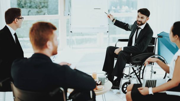 Person in Wheelchair. Man Shows Pointer. Panoramic View. Disabled Workers Talking. People with Limited Opportunities. Work Meeting. Business Clothes. Business Suits. Business Lunch. Man in Wheelchair. - Foto, Imagen