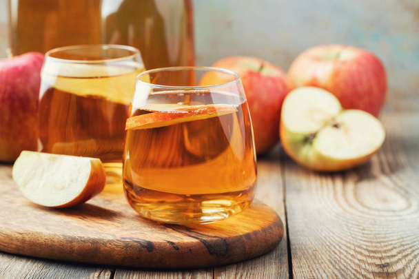 Organic Apple cider or juice on a wooden table. Two glasses with drink and autumn leaves on rustic background - Photo, image