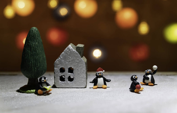 Pinguins em diferentes atuações ao redor da casa e da árvore no chão de gelo
 - Foto, Imagem