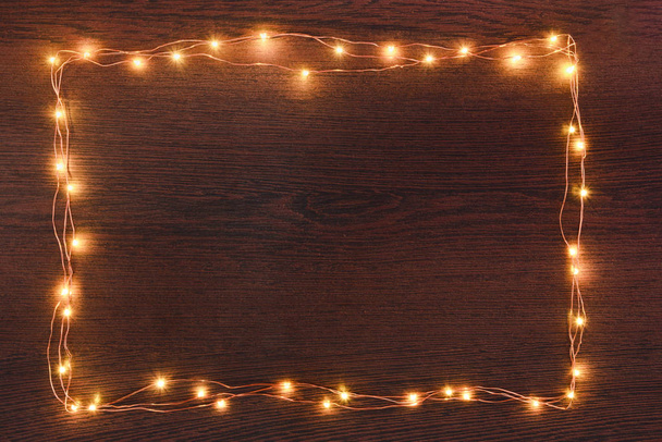 Karácsonyi fények garland határ felett a sötét fából készült háttér. Lapos feküdt, másol hely. - Fotó, kép