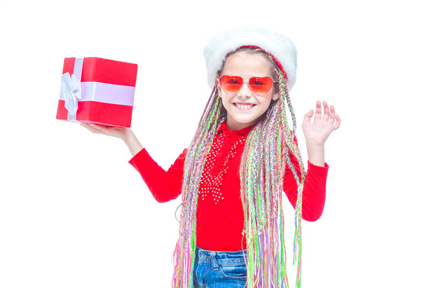 Girl in Santas hat. Portrait of little cute girl holding box of Christmas present, Small girl hug her gift with happy and fun expression isolated on white background. Holiday gift - Photo, Image