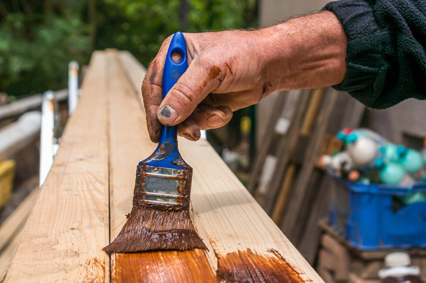 Художник с кистью для покраски деревянной поверхности для защиты древесины от внешних воздействий
 - Фото, изображение