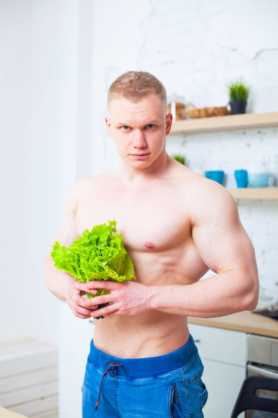 Gespierde man met een naakte torso in de keuken met een salade, begrip van gezond eten. Atletische manier van leven. - Foto, afbeelding