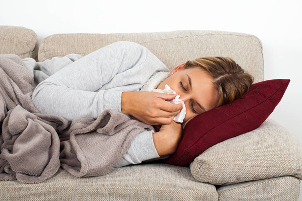 Sick woman lying on the sofa blowing her nose - sinus infection - Фото, изображение