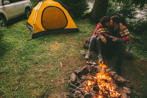 couple assis près du feu de camp et boire du thé et raconter des histoires. tente et SUV sur fond. union avec la nature
 - Photo, image