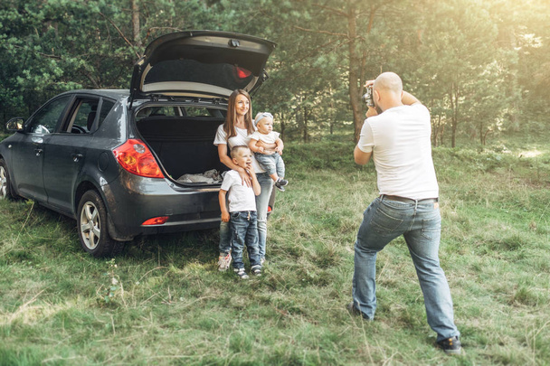 Pareja joven con sus hijos pequeños haciendo picnic en el bosque, concepto de fin de semana familiar, cuatro personas disfrutando del verano
 - Foto, Imagen