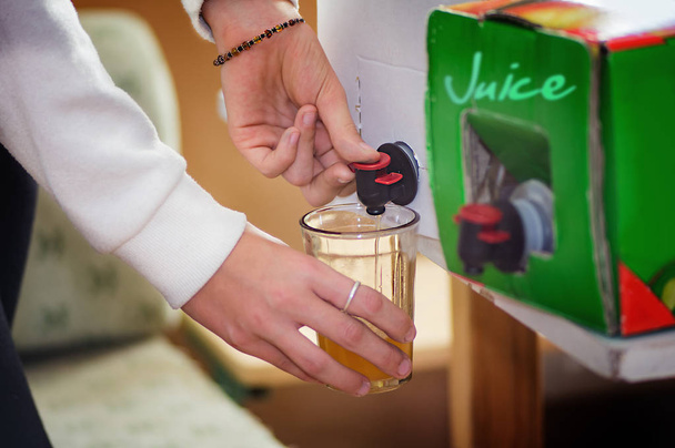 Bag with juice in box for packaging with valve and spout. Girl taking juice from it to glass.  - Fotografie, Obrázek