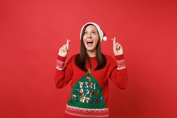 Merry Santa κορίτσι κοιτώντας ψηλά, κρατώντας τα δάχτυλα διέσχισαν, στόμα ορθάνοιχτο, αναμονή για ξεχωριστή στιγμή απομονωμένος σε κόκκινο φόντο. Ευτυχισμένο το νέο έτος 2019 γιορτή διακοπών κόμμα έννοια. Κοροϊδεύετε αντίγραφο χώρου - Φωτογραφία, εικόνα