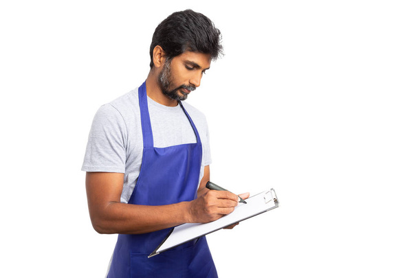 Store manager or indian owner writing on paper checklist clipboard with focused look isolated on white studio background - Photo, Image