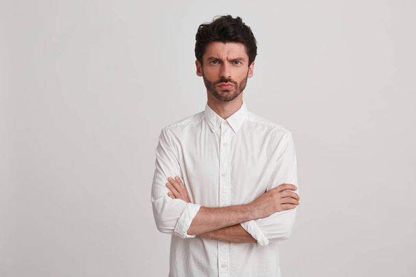 Clouse-se de um jovem atraente vestindo camisa branca clássico longsleave olhando sério e focado, mantém os braços cruzados com um isolado sobre fundo branco
 - Foto, Imagem