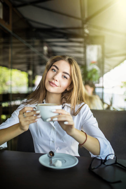 Portrait of happy young business woman with mug in hands drinking coffee in morning at restaurant - Foto, Imagen