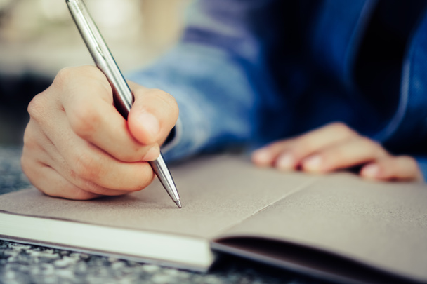 Αντιγράψτε χώρο της γυναίκας χέρι γράφοντας σε λευκό σημειωματάριο με πολύχρωμο φόντο bokeh. - Φωτογραφία, εικόνα