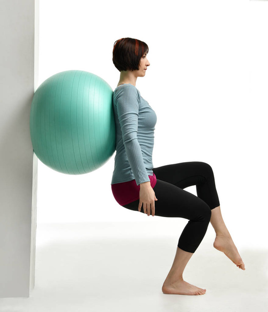 Female fitness instructor holds legs in gym and workout exercises for abdominals with green sport ball over white - Foto, immagini
